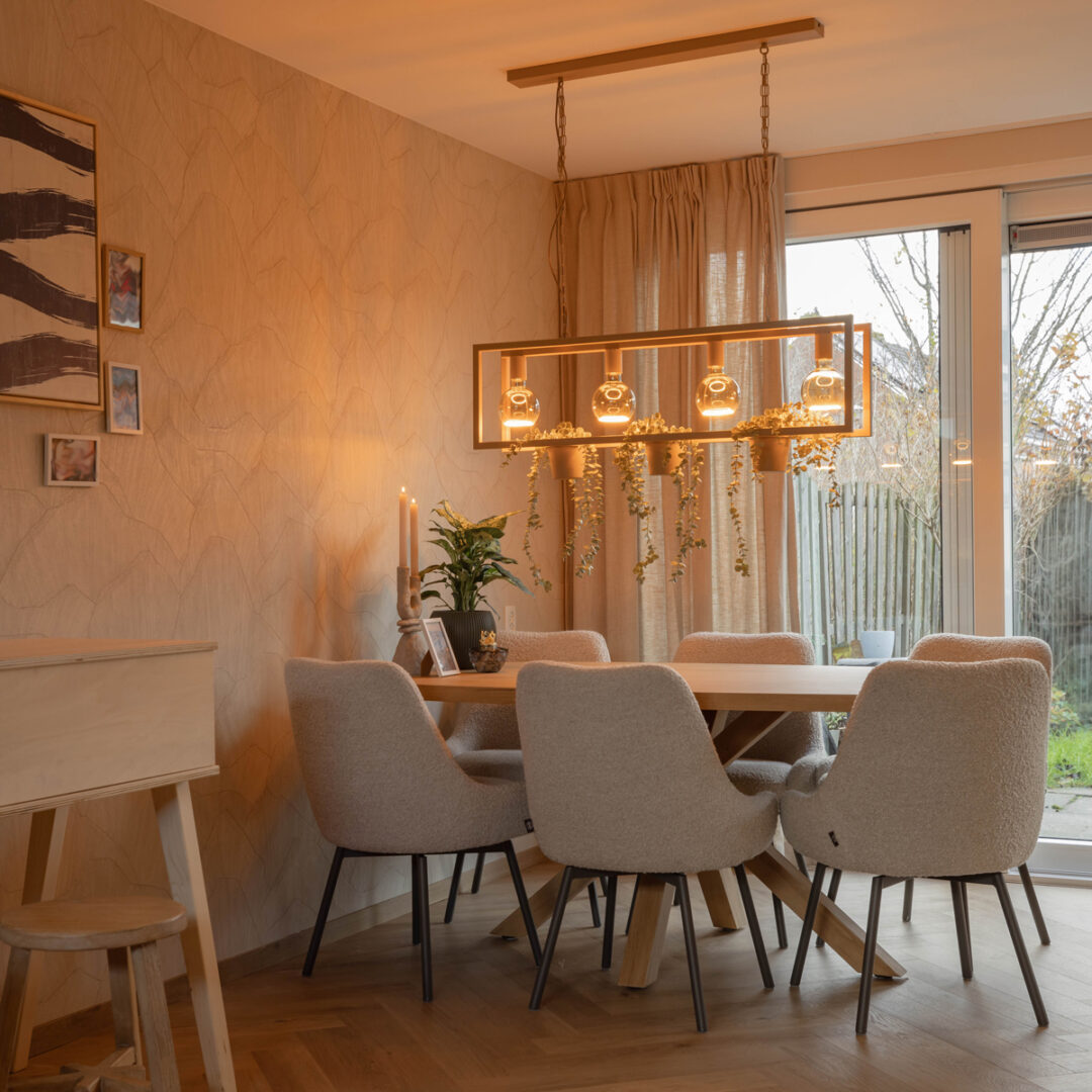 Rechthoekige hanglamp van Straluma met vier glazen lichtpunten boven een houten eettafel met beige stoelen in een lichte, warme eetkamer.