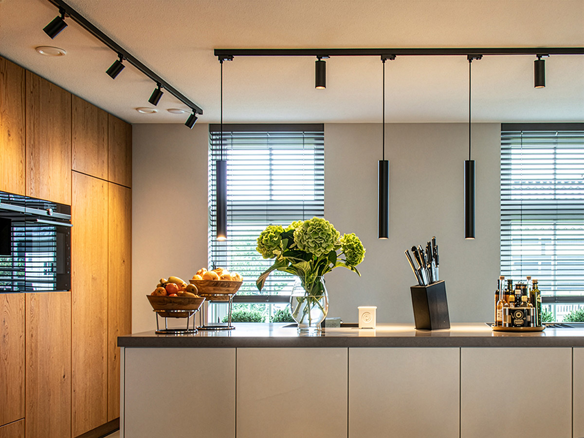 Moderne keuken met zwarte spotrails, slanke hanglampen boven het kookeiland en houten accenten.