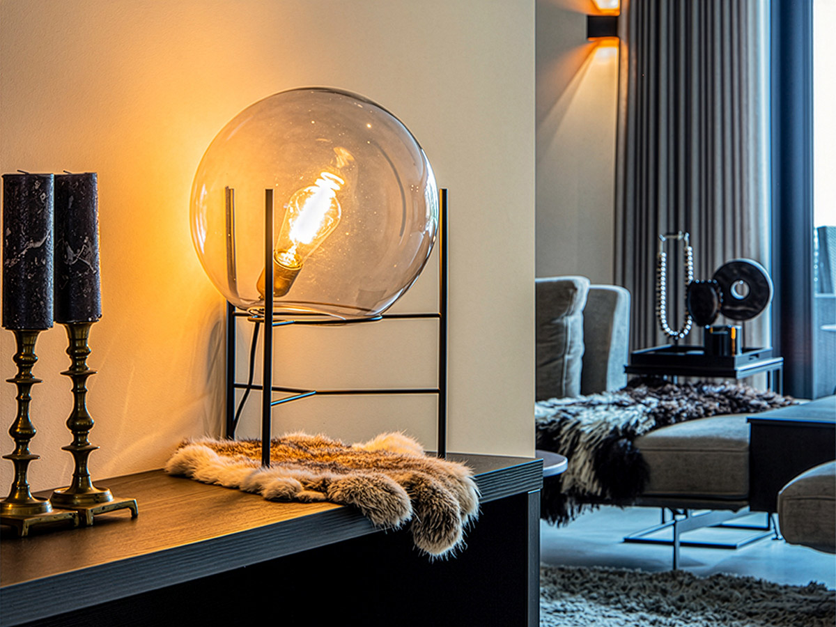 Glazen tafellamp met warme lichtbron op een zwarte sidetable in een modern, sfeervol interieur