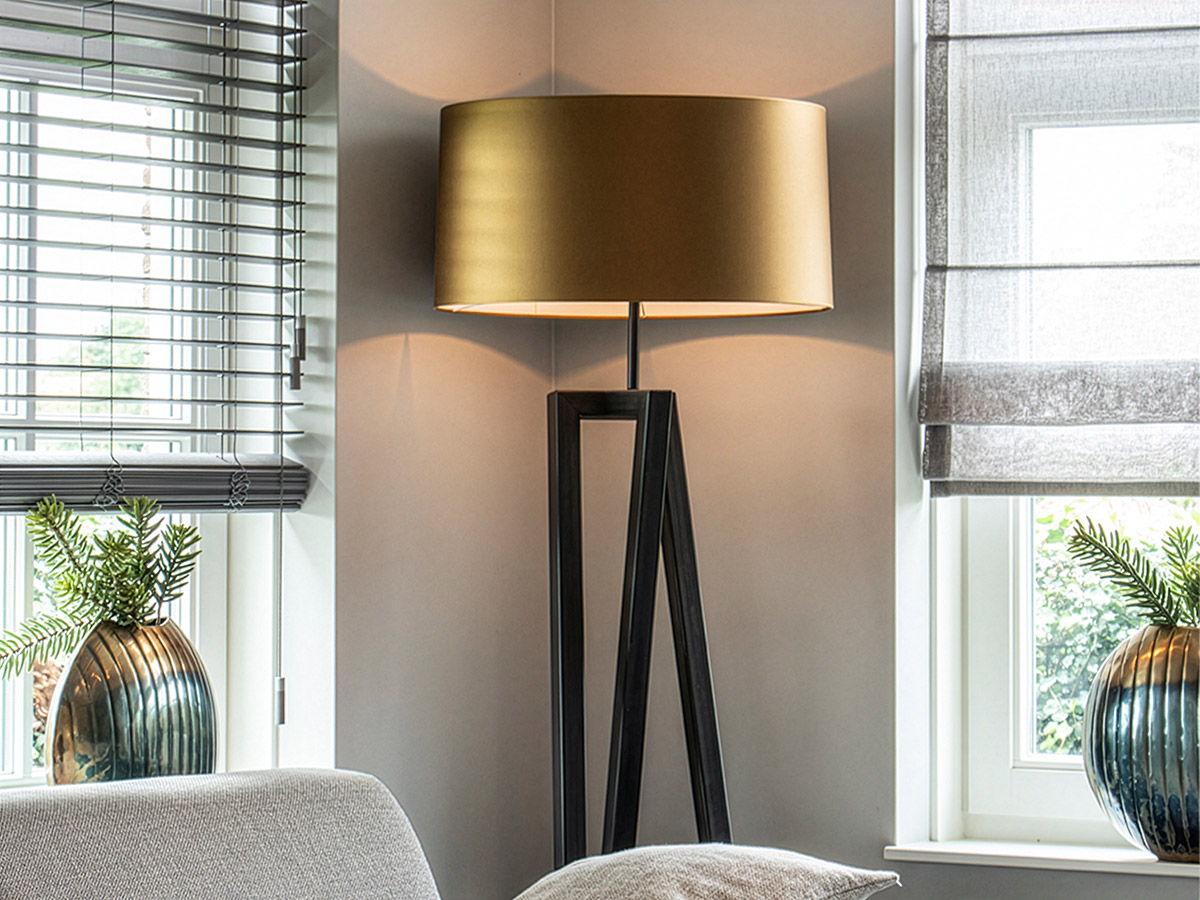 Moderne vloerlamp met goudkleurige lampenkap in een stijlvolle woonkamer met grote ramen en decoratieve vazen.