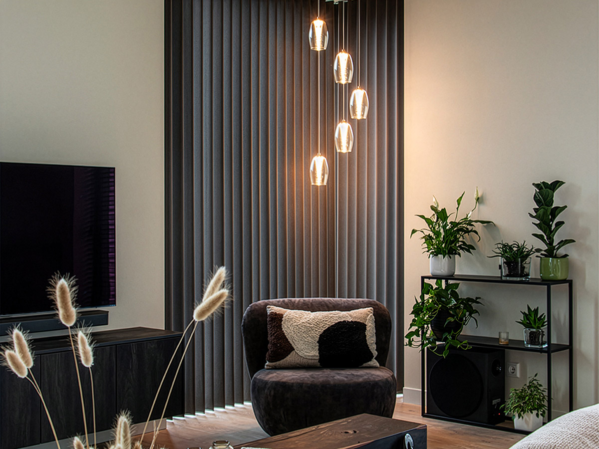 Moderne woonkamer met stijlvolle hanglamp en zwarte fauteuil, sfeervol ingericht met groene kamerplanten – Straluma