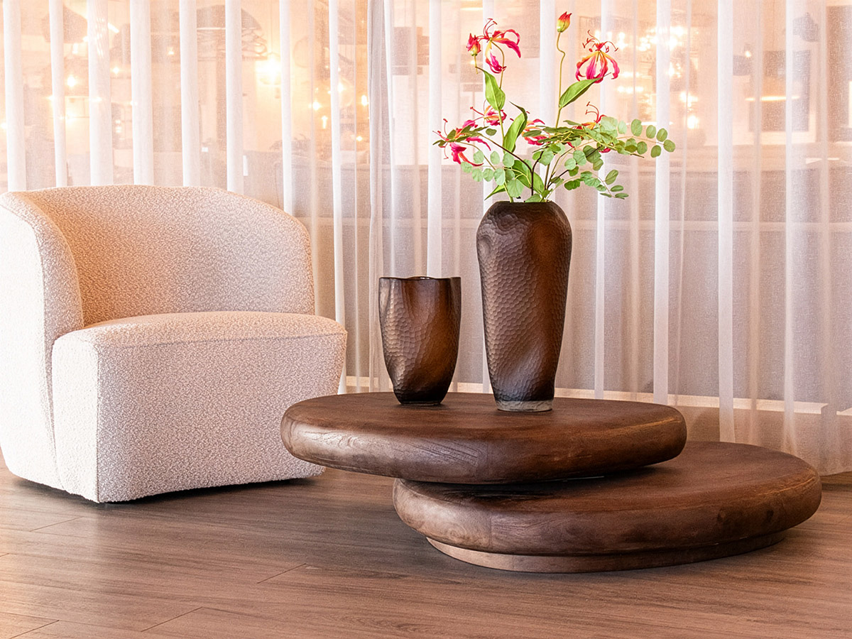 Bouclé fauteuil met ronde houten salontafels en decoratieve vazen in warm modern interieur