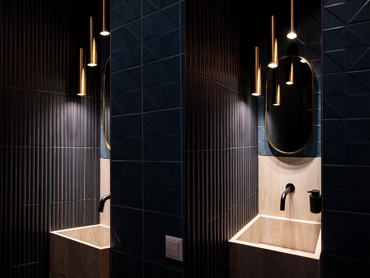 Slanke gouden hanglampen boven een waskom met donkere wandtegels, luxe verlichting ontworpen door Straluma.