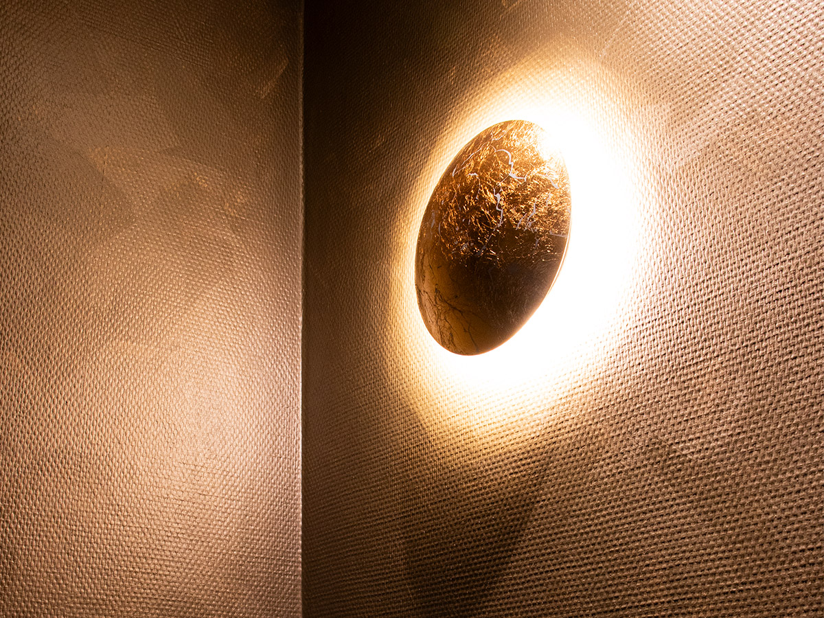 Ronde decoratieve wandlamp met warme gloed op structuurmuur in Het Wapen van Rhoon, geleverd door Straluma.